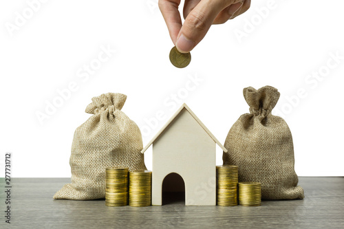 Saving money or property investment or buy a new home concept. A small house model with stack of coins and money bag on wood table. Depicts sustainable financial goal.