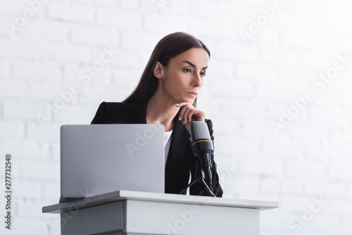 pensive lecturer standing on podium tribune near microphone and laptop photo