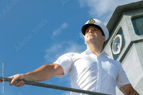 Captain standing on the gallery of navigation bridge of ship and  looking ahead. A sailor officer in white uniform stands aboard a ship. photo