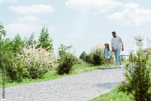 handsome father and daughter walking near green plants and holding hands © LIGHTFIELD STUDIOS