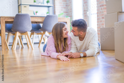 Young beautiful couple in love moving to new home, lying on the floor around cardboard boxes, very happy and cheerful for new apartment