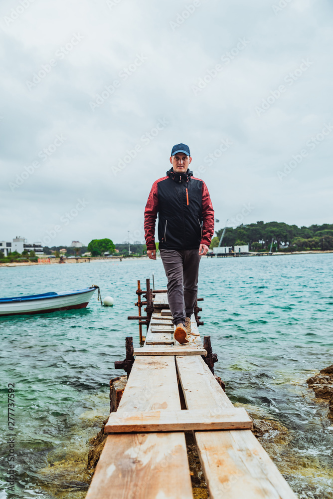 man walking by small wooden pier overcast weather stormed sea on background