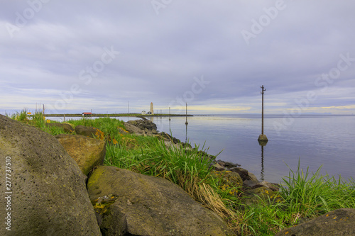 Electricity pylons in the water to the island of Grotta near Reykjavik in the morning with clouds in the sky. in the background uninhabited lighthouse and houses of Iceland