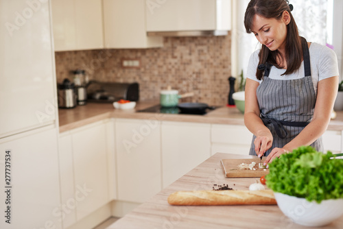 Smiling Caucasian female chef in apron chopping leek in kitchen and preparing dinner. Preparation of domestic food concept.
