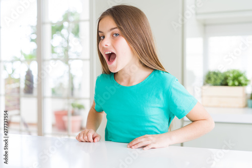 Beautiful young girl kid wearing green t-shirt afraid and shocked with surprise expression, fear and excited face.