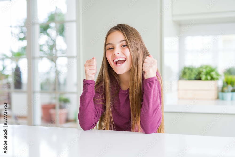 Beautiful young girl kid on white table excited for success with arms raised celebrating victory smiling. Winner concept. Beautiful young girl kid on white table excited for success with arms raised celebrating victory smiling. Winner concept.