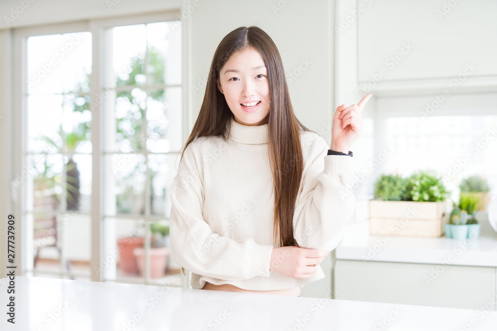 Beautiful Asian woman wearing casual sweater with a big smile on face, pointing with hand and finger to the side looking at the camera. Beautiful Asian woman wearing casual sweater with a big smile on face, pointing with hand and finger to the side looking at the camera.