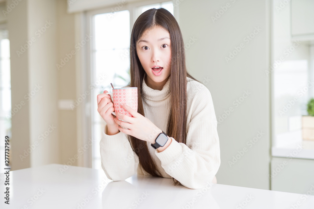 Beautiful Asian woman drinking a cup of coffee scared in shock with a surprise face, afraid and excited with fear expression Beautiful Asian woman drinking a cup of coffee scared in shock with a surprise face, afraid and excited with fear expression
