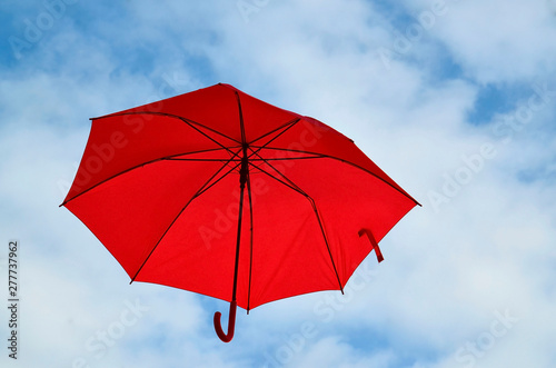 Red umbrella floating in the air on a blue cloudy sky background with space for text.