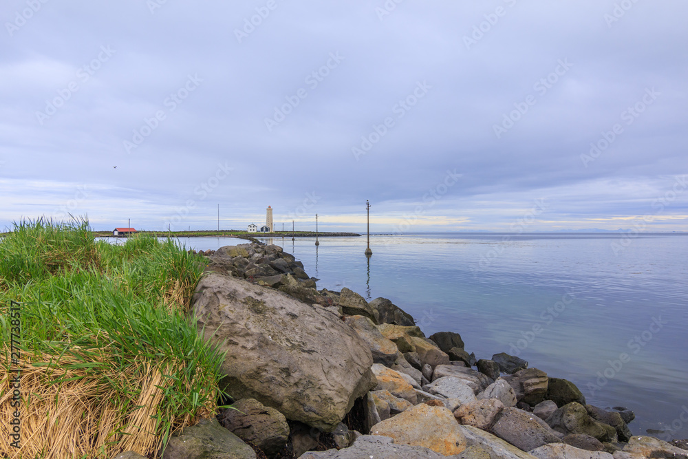 Island Grotta near Reykjavik in the morning with clouds in the sky. Lighthouse and houses in the background with bird sanctuary on the side of power pylons in the water to the peninsula