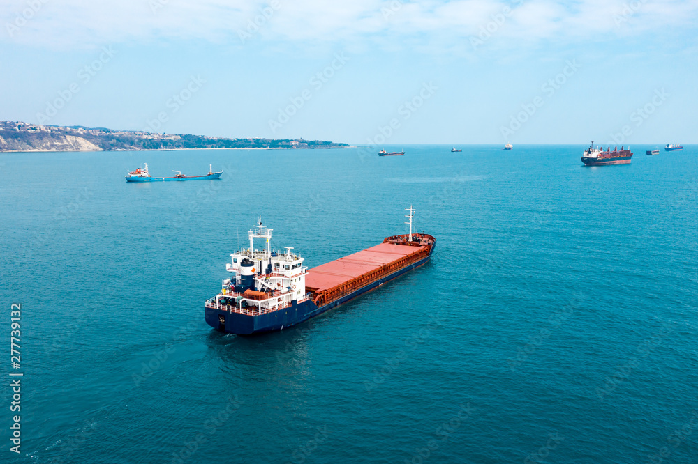 Aerial view of high-speed sea vessel for transportation of a cargo vessel at high speed is drifting near the seaport of the city at sunset. Ship on the background of blue sea water. Import, export