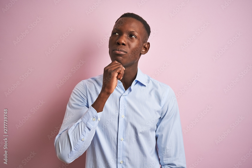 African american man wearing blue elegant shirt standing over isolated pink background with hand on chin thinking about question, pensive expression. Smiling with thoughtful face. Doubt concept. African american man wearing blue elegant shirt standing over isolated pink background with hand on chin thinking about question, pensive expression. Smiling with thoughtful face. Doubt concept.