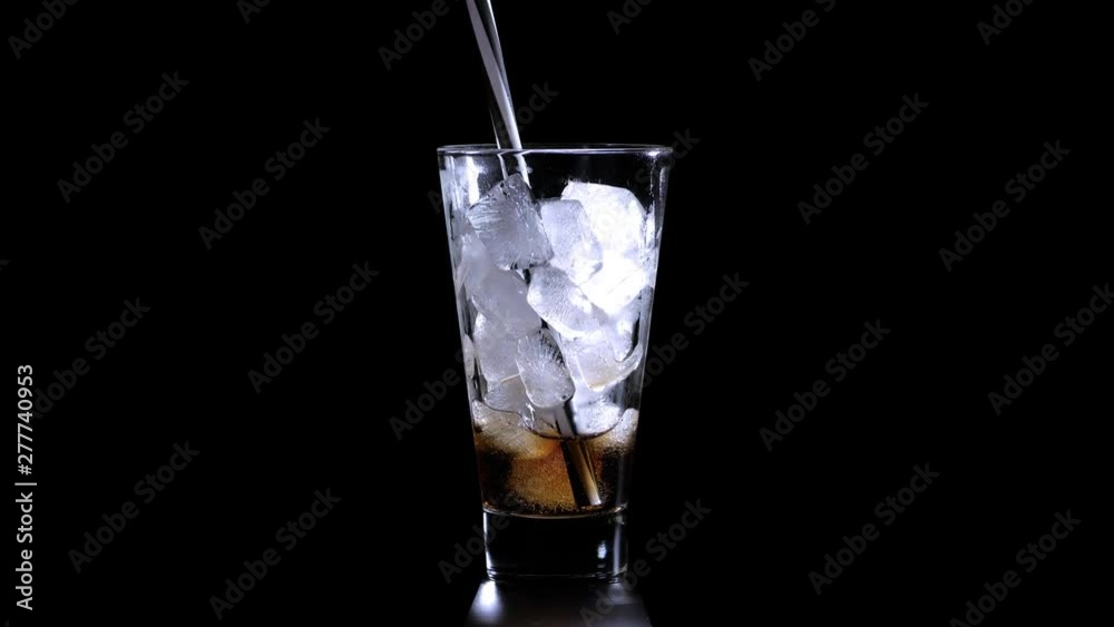 Pouring Cola with ice cubes. Cola drink with Ice and bubbles and water drops on glass. Soda closeup. Cola on a black background. 4K. Copy space for your text. Footage is perfect for the layer with