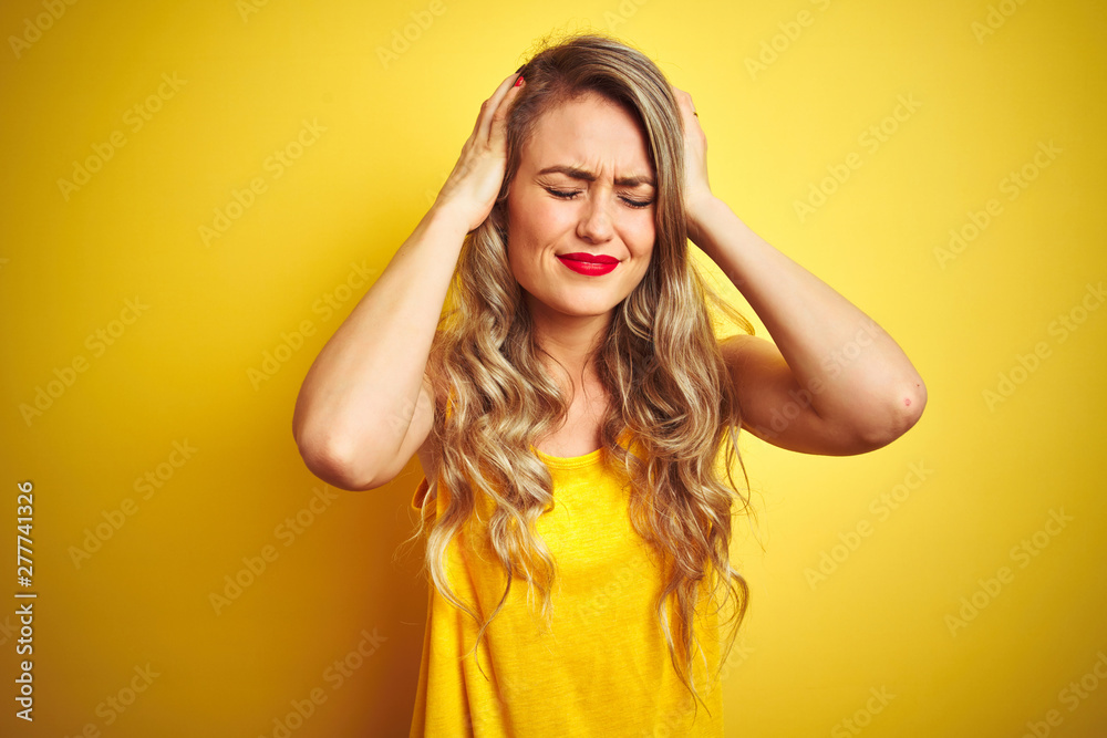 Fototapeta premium Young beautiful woman wearing t-shirt standing over yellow isolated background suffering from headache desperate and stressed because pain and migraine. Hands on head.
