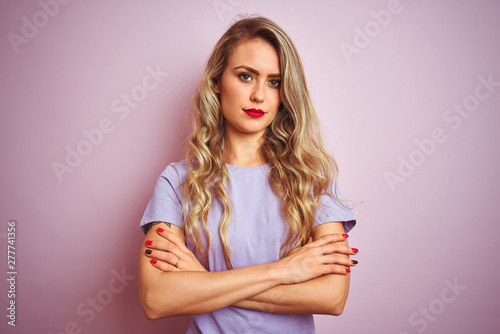 Young beautiful woman wearing purple t-shirt standing over pink isolated background skeptic and nervous, disapproving expression on face with crossed arms. Negative person.