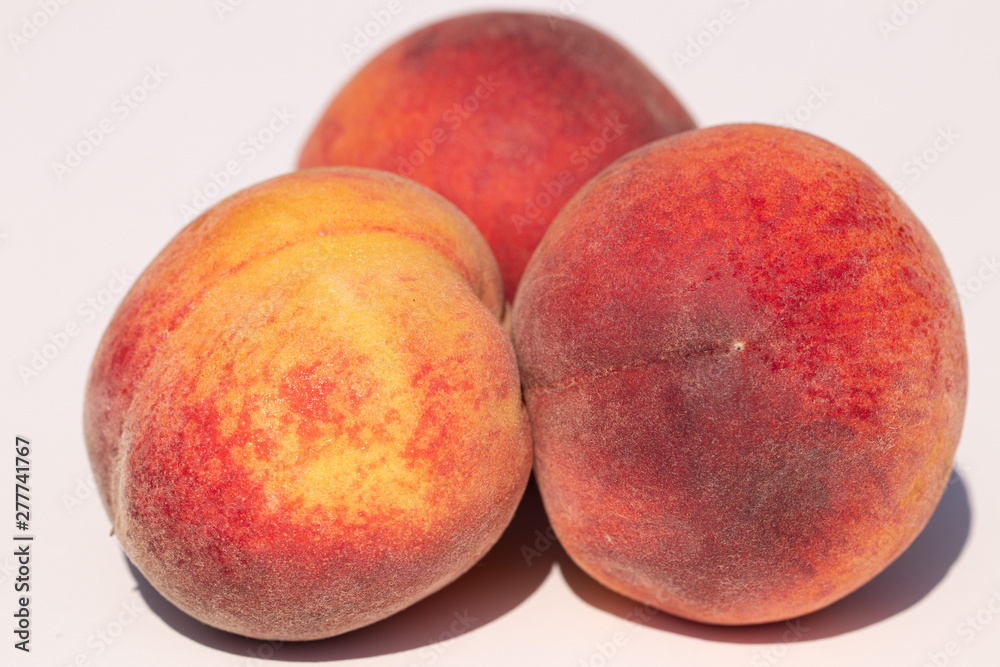 Three juicy peaches on a white background in sunlight Three juicy peaches on a white background in sunlight
