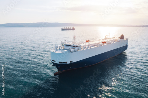 Aerial view of high-speed sea vessel for transportation of cargo vessel at high speed is drifting near the seaport of the city at sunset. Ship on the background of blue sea water. Import, export. Top