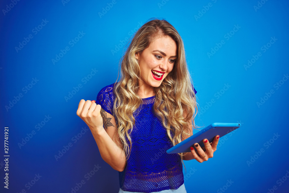 Young beautiful woman using tablet over blue isolated background screaming proud and celebrating victory and success very excited, cheering emotion Young beautiful woman using tablet over blue isolated background screaming proud and celebrating victory and success very excited, cheering emotion