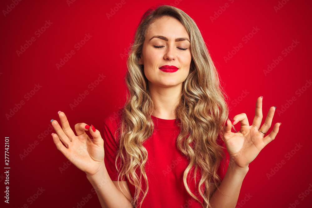 Young beautiful woman wearing basic t-shirt standing over red isolated background relax and smiling with eyes closed doing meditation gesture with fingers. Yoga concept. Young beautiful woman wearing basic t-shirt standing over red isolated background relax and smiling with eyes closed doing meditation gesture with fingers. Yoga concept.