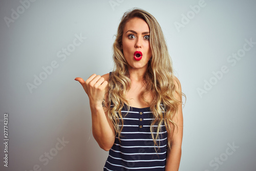 Young beautiful woman wearing stripes t-shirt standing over white isolated background Surprised pointing with hand finger to the side, open mouth amazed expression.