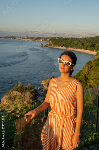 Travel destination in Bali. Rare view of brunette woman in summer dress stand at viewpoint from high cliff.
