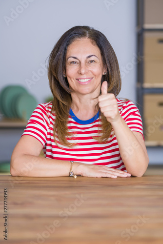 Middle age senior woman sitting at the table at home doing happy thumbs up gesture with hand. Approving expression looking at the camera with showing success.