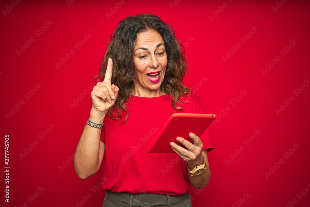 Middle age senior woman using touchpad tablet over red isolated background surprised with an idea or question pointing finger with happy face, number one Middle age senior woman using touchpad tablet over red isolated background surprised with an idea or question pointing finger with happy face, number one