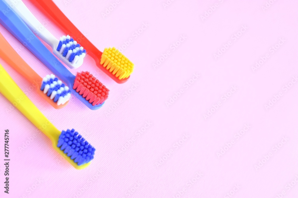 Row of Colorful toothbrushes with selective focus on blurred pink background. Dental tools for daily teeth protection. Multicolored plastic toothbrush with bright bristles with soft focus. Oral hygien Row of Colorful toothbrushes with selective focus on blurred pink background. Dental tools for daily teeth protection. Multicolored plastic toothbrush with bright bristles with soft focus. Oral hygien