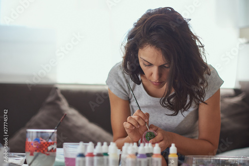  Brunette woman of latin race painting small figures with a white background.