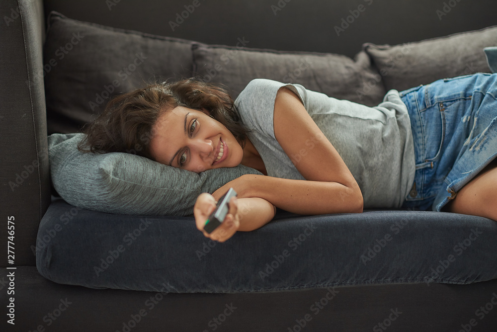 Brunette woman of Latin origin in an armchair with the control of the television in her hand. Brunette woman of Latin origin in an armchair with the control of the television in her hand.