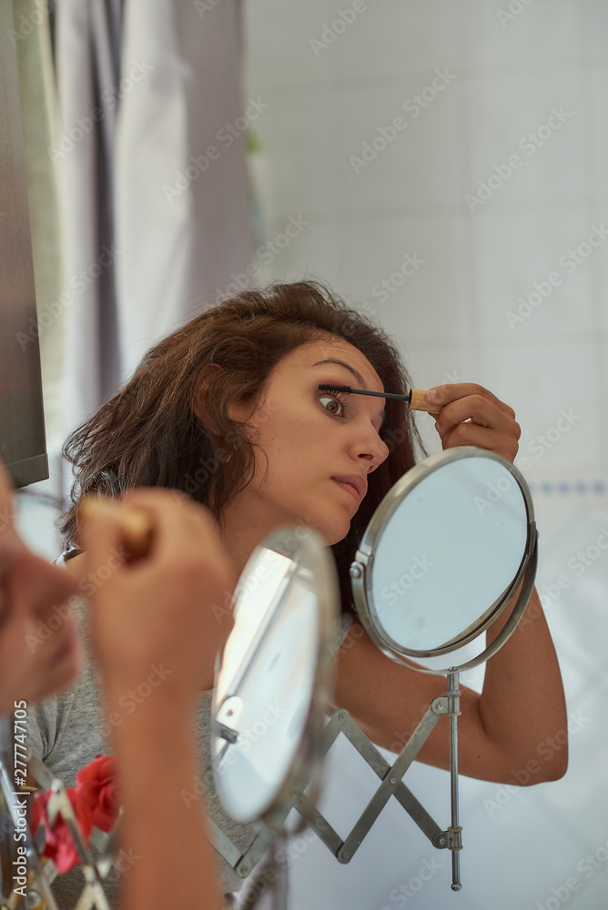  Brunette woman of latin race doing makeup in a mirror.