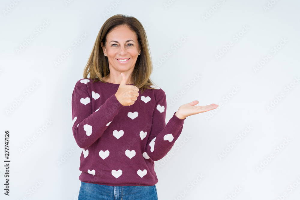 Beautiful middle age woman wearing heart sweater over isolated background Showing palm hand and doing ok gesture with thumbs up, smiling happy and cheerful Beautiful middle age woman wearing heart sweater over isolated background Showing palm hand and doing ok gesture with thumbs up, smiling happy and cheerful