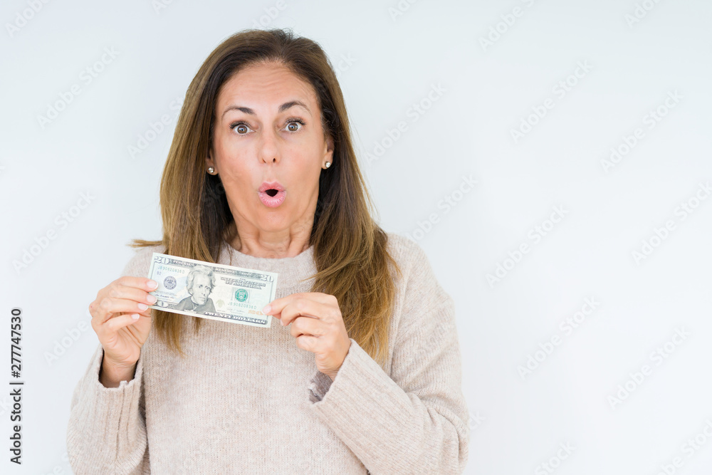 Middle age woman holding 20 dollars bank note over isolated background scared in shock with a surprise face, afraid and excited with fear expression Middle age woman holding 20 dollars bank note over isolated background scared in shock with a surprise face, afraid and excited with fear expression