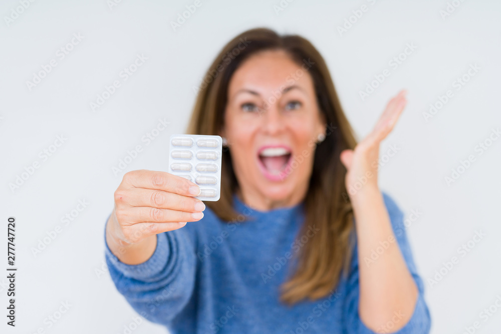 Middle age woman holding pharmaceutical pills over isolated background very happy and excited, winner expression celebrating victory screaming with big smile and raised hands Middle age woman holding pharmaceutical pills over isolated background very happy and excited, winner expression celebrating victory screaming with big smile and raised hands