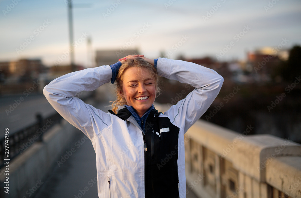 A blonde female runner smiles after a run on the Monroe Street Bridge adjacent a roaring Spokane Falls at high spring flow near downtown Spokane, Washington at sunset. A blonde female runner smiles after a run on the Monroe Street Bridge adjacent a roaring Spokane Falls at high spring flow near downtown Spokane, Washington at sunset.