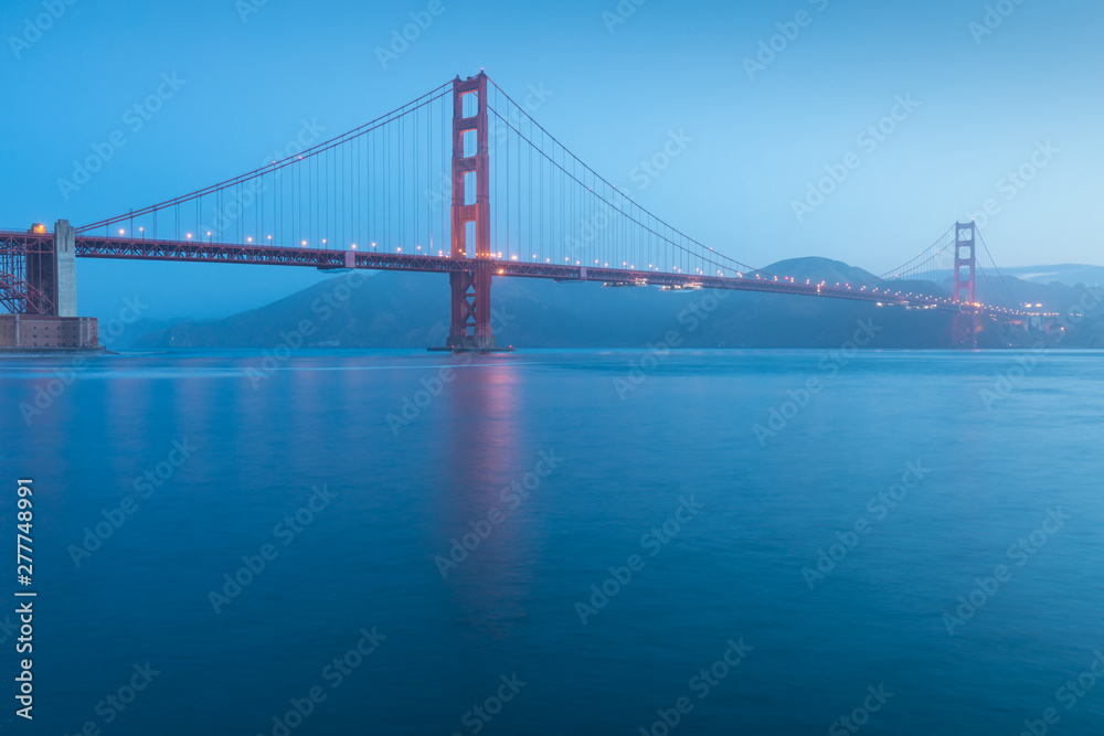 Classic panoramic view of famous Golden Gate Bridge seen from San Francisco harbour in beautiful evening light on a dusk with blue sky and clouds and fog in summer, San Francisco, California, USA