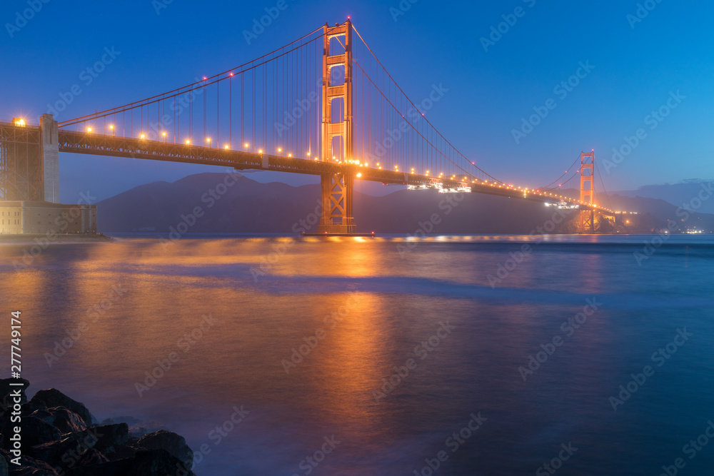 Obraz premium Classic panoramic view of famous Golden Gate Bridge seen from San Francisco harbour in beautiful evening light on a dusk with blue sky and clouds and fog in summer, San Francisco, California, USA