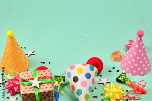 Birthday caps, present, confetti, ribbons, stars, clown noses on a green background. Space for text or design.