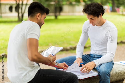 Two students studying together sitting on a bench outdoor