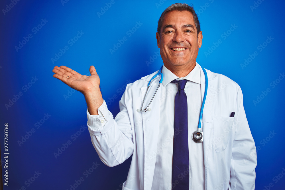 Handsome middle age doctor man wearing stethoscope over isolated blue background smiling cheerful presenting and pointing with palm of hand looking at the camera.