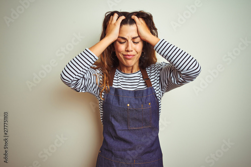 Obraz na plátně Young beautiful chef woman wearing apron cooking over white isolated background suffering from headache desperate and stressed because pain and migraine