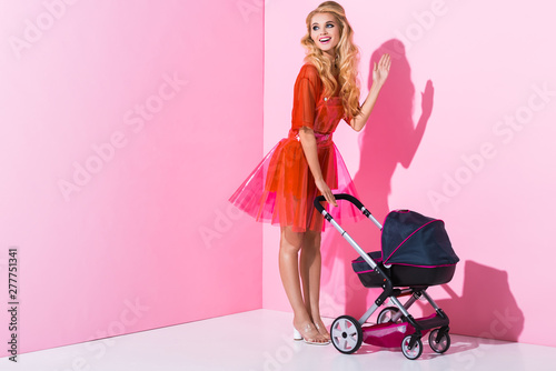 beautiful girl with baby stroller waving on pink, doll concept