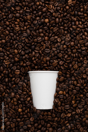White disposable cup of coffee to go on the background of roasted beans.