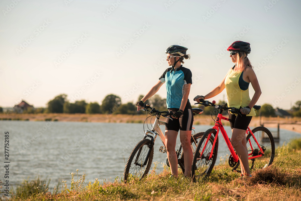 Two women cyclists with bikes standing and talking at the lake shore
