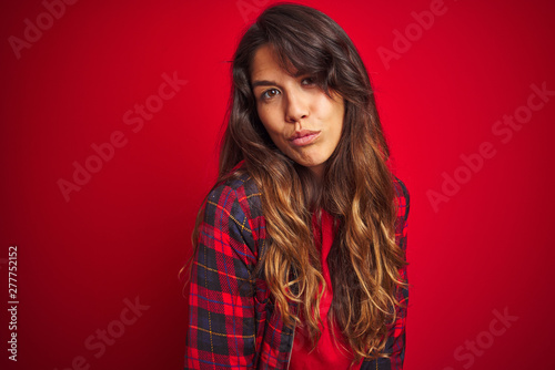Young beautiful woman wearing casual jacket standing over red isolated background showing arms muscles smiling proud. Fitness concept.