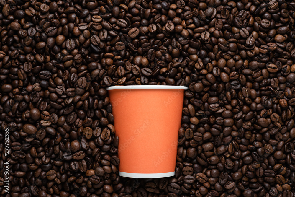 Fototapeta premium Orange disposable cup of coffee to go on the background of roasted beans.