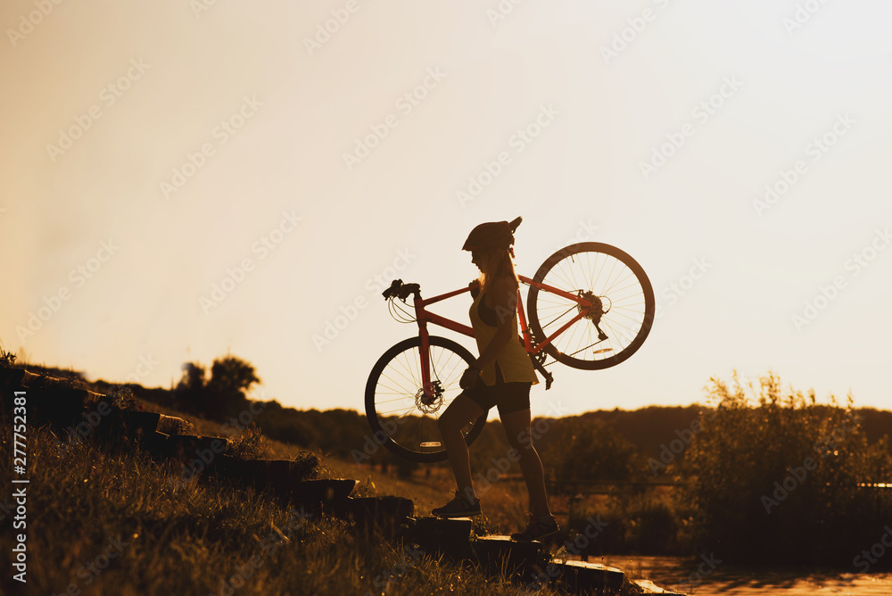 Silhouette of a woman carrying a bike against evening sky