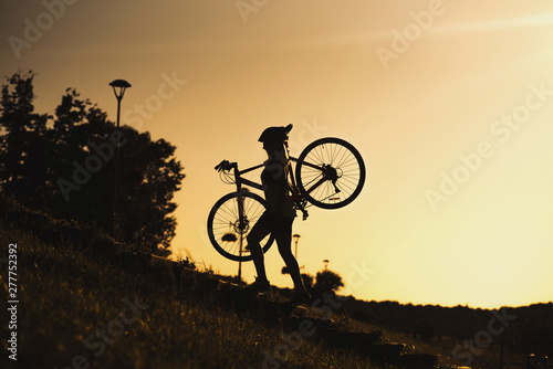 Silhouette of a woman carrying a bike against evening sky