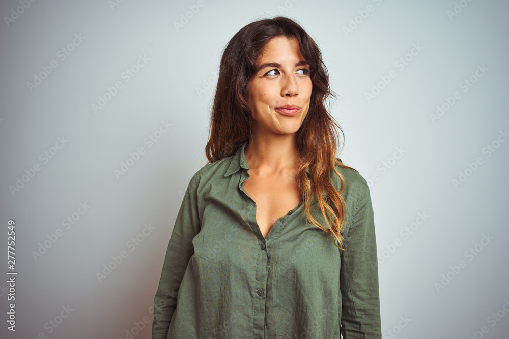 Young beautiful woman wearing green shirt standing over grey isolated background smiling looking to the side and staring away thinking. Young beautiful woman wearing green shirt standing over grey isolated background smiling looking to the side and staring away thinking.