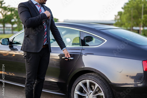 Handsome young chauffeur holding the door of a car